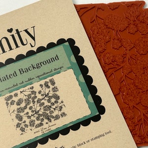 May include: A close-up of a red rubber stamp with a floral design. The stamp is labeled "Floriated Background" and is pre-cut and un-mounted. The stamp is from the Unity brand.