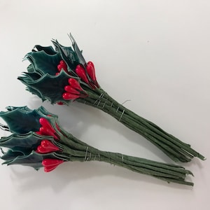 May include: Two bunches of artificial holly sprigs with red berries. Each bunch has green leaves and stems.
