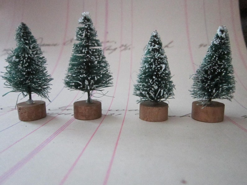Peut inclure: Quatre petits sapins de No&euml;l artificiels avec des branches vertes recouvertes de neige floqu&eacute;e blanche. Les sapins sont sur des socles en bois brun.