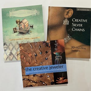 May include: Three jewelry-making books are displayed. The books are titled "Pretty Little Things", "Creative Silver Chains", and "The Creative Jeweler". The "Creative Silver Chains" book features a woman wearing silver earrings and a necklace. The other books have jewelry on the cover.