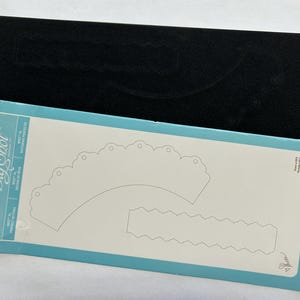 May include: A die-cutting template for a setting basket, featuring a scalloped edge and a straight edge. The template is labeled "Setting Basket" and is part of the "Big Shot" collection.