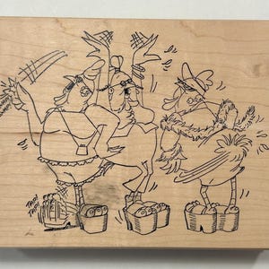 May include: Wooden stamp featuring a humorous cartoon illustration of three anthropomorphic birds. The birds are depicted in various poses, with speech bubbles that say "SNAP!" and "TAP!". The stamp is made of light-colored wood.