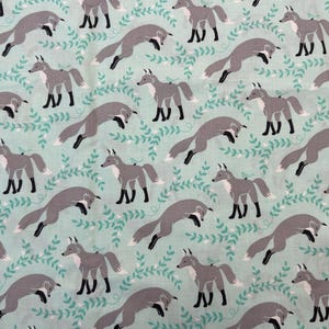 May include: Fabric with a repeating pattern of gray foxes in various poses, set against a light teal background with teal-colored leafy vines. The foxes have black paws and white-tipped tails.