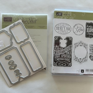 Puede incluir: Un juego de troqueles Big Shot de metal y una funda de plástico transparente que contiene sellos de goma. Los troqueles tienen varias formas de etiquetas. Los sellos incluyen frases como "Happy Big Day!" y "I can't thank you enough."
