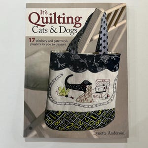 May include: A book titled "It's Quilting Cats & Dogs" with a tote bag featuring a black dog and sewing machine design. The bag has a black and white floral pattern and a number pattern at the bottom. The book cover also has the text "17 stitchery and patchwork projects for you to treasure."