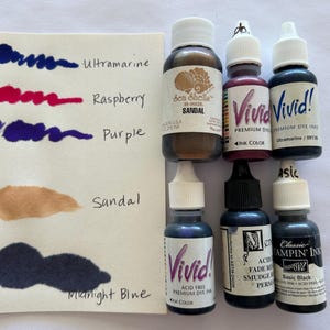 May include: An assortment of ink bottles and ink swatches. The swatches display colors like ultramarine, raspberry, purple, and midnight blue. The ink bottles are labeled with names like "Vivid!" and "Classic Stampin' Ink".