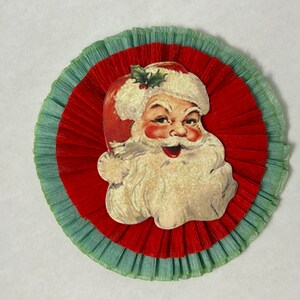 May include: A red and green paper Christmas ornament featuring a vintage illustration of Santa Claus's face.