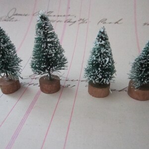 Peut inclure: Quatre mini sapins de No&euml;l artificiels avec des aiguilles vertes et un flocage blanc, chacun sur un socle en bois brun.