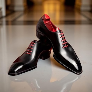 May include: A pair of black leather dress shoes with red laces and interior lining. The shoes have a polished, glossy finish and are set against a neutral background, showcasing their elegant design.
