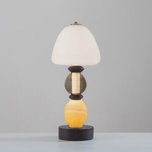 May include: A modern table lamp with a white, rounded shade. The lamp features a stacked design with a dark brown base, a yellow and orange lower section, a gray middle section, and a dark brown top section. The lamp sits on a black circular base.