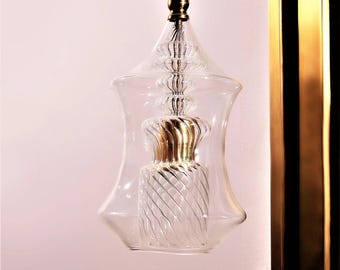 May include: A clear glass and gold-toned wall sconce with a decorative design. The sconce features a clear glass shade with a spiral design and a gold-toned metal frame. The sconce is mounted on a wall with a gold-toned metal backing.