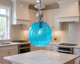 May include: A blue glass pendant light fixture with a spherical shade and a decorative top. The shade has a spiral design and hangs above a white kitchen island. The fixture is suspended from the ceiling.