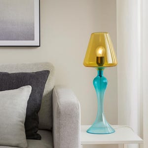 May include: A vibrant table lamp with a yellow lampshade and a turquoise base. The lamp features a classic design with a bulb inside the shade. The lamp is placed on a white table next to a gray sofa.