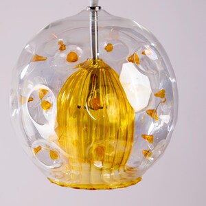 Puede incluir: Una lámpara colgante de globo de vidrio transparente con una pantalla de vidrio amarillo acanalado en el interior. El globo tiene pequeñas burbujas de vidrio transparentes en la superficie.