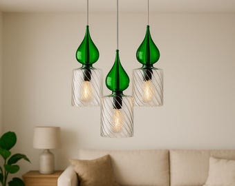May include: Three pendant lights with green glass tops and clear, cylindrical glass shades with a spiral design. The lights hang from a gold-colored ceiling fixture. The bulbs are visible inside the shades.