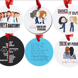 May include: A set of six round Christmas ornaments with red ribbons. The ornaments feature images and text from the TV show "Grey's Anatomy." Designs include characters, quotes, and the show's logo. The ornaments are white, black, and blue.