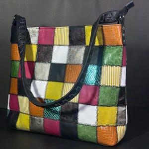 Può includere: Una borsa tote patchwork con una tracolla nera. La borsa è realizzata con quadrati di pelle di diversi colori, tra cui rosso, verde, giallo, bianco e nero.
