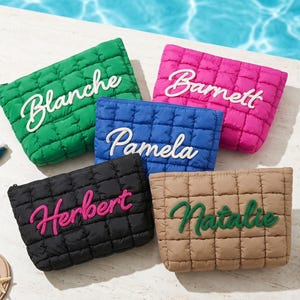 May include: Five quilted cosmetic bags in green, pink, blue, black, and tan. Each bag features an embroidered name in a contrasting colour: Blanche, Barnett, Pamela, Herbert, and Natalie. The bags are displayed near a swimming pool.