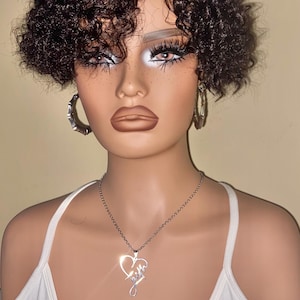 May include: A mannequin head with dark brown curly hair, wearing silver hoop earrings and a silver necklace with a heart pendant that says "faith". The mannequin is wearing a white tank top.