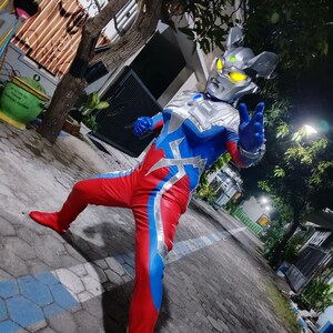 K&ouml;nnte beinhalten: Ein Ganzk&ouml;rperkost&uuml;m mit einem silbernen Helm mit gelben Augen, einem blau-roten Body mit silbernen Akzenten und roten Stiefeln. Das Kost&uuml;m ist so gestaltet, dass es einem Superhelden-Charakter &auml;hnelt.