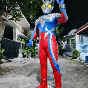 K&ouml;nnte beinhalten: Ein rot, blau und silberfarbenes Superheldenkost&uuml;m. Das Kost&uuml;m hat einen silbernen Helm mit gelben Augen und eine blaue Handgeste. Das Outfit umfasst rote Stiefel und Handschuhe.