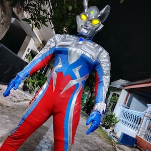 K&ouml;nnte beinhalten: Ein Ganzk&ouml;rperkost&uuml;m mit einem silber-blauen Helm mit gelben Augen und einem rot-blau-silbernen Body. Das Kost&uuml;m beinhaltet blaue Handschuhe und ein silbernes Armband. Das Gesamtdesign ist futuristisch und superhero-Themen.