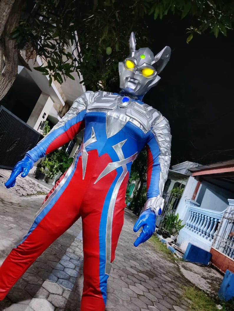 K&ouml;nnte beinhalten: Ein Ganzk&ouml;rperkost&uuml;m mit einem silber-blauen Helm mit gelben Augen und einem rot-blau-silbernen Body. Das Kost&uuml;m beinhaltet blaue Handschuhe und ein silbernes Armband. Das Gesamtdesign ist futuristisch und superhero-Themen.