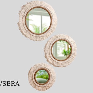May include: Three round mirrors with a bohemian design. Each mirror has a natural rope frame, surrounded by a cream-colored fringe. The mirrors are of varying sizes and are arranged in a cascading pattern. The text "EVSERA" is at the bottom.
