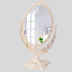 Peut inclure: Un miroir de courtoisie ovale blanc cassé avec un design floral orné. Le miroir est double face et repose sur un socle décoratif. Le cadre et la base présentent des sculptures complexes, ajoutant une esthétique vintage. Idéal pour une chambre ou une salle de bain.