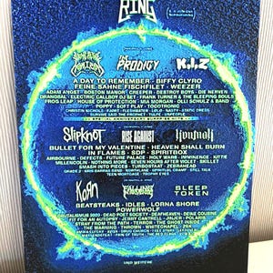 May include: A Rock am Ring concert poster with a blue and green design, listing bands such as Slipknot, The Prodigy, and Korn. The poster has a circular layout, with band names arranged around a central design element.
