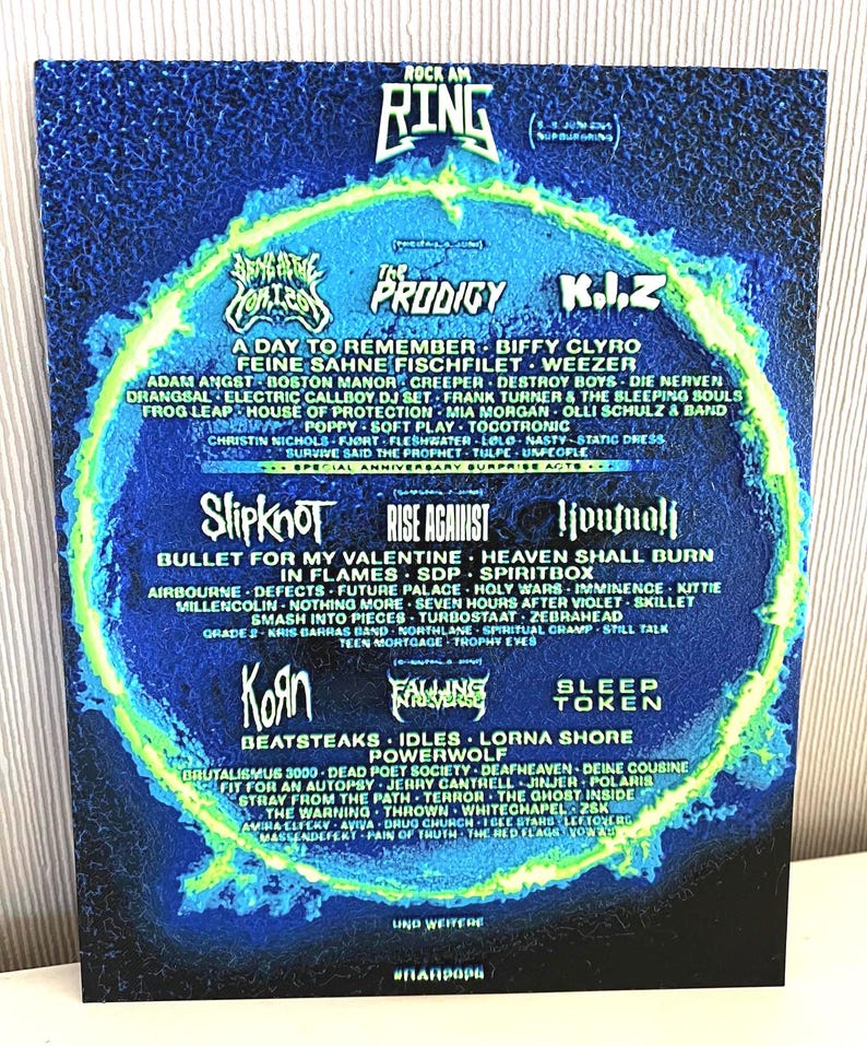 May include: A Rock am Ring concert poster with a blue and green design, listing bands such as Slipknot, The Prodigy, and Korn. The poster has a circular layout, with band names arranged around a central design element.