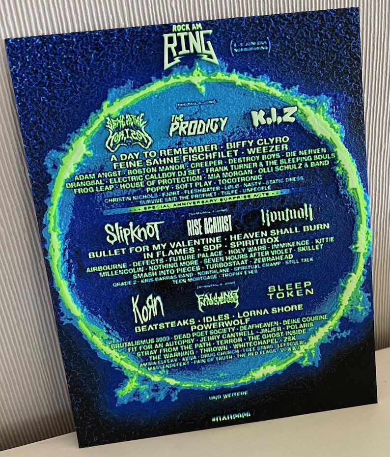 May include: A Rock am Ring festival poster with a dark blue and green colour scheme. The poster lists bands such as Slipknot, Korn, and The Prodigy. The text is white and arranged in a circular format.