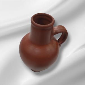 May include: A handmade, brown ceramic pitcher with a rounded body and a handle. The pitcher has a wide opening and a smooth, unglazed surface. The design is simple and rustic, suitable for serving water or other beverages.