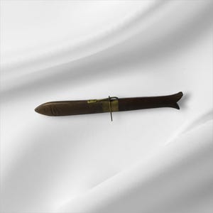 May include: A brown, fish-shaped knife with a brass clasp and a dark handle. The knife has a small, carved fish head at the tip and a fin-like shape at the end. The knife is approximately 10 inches long.
