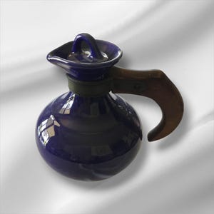 May include: A cobalt blue ceramic coffee pot with a wooden handle. The pot has a round body, a spout, and a lid with a small handle. The handle is made of dark wood and is attached to the pot with metal rivets.