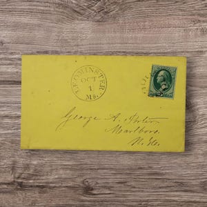 May include: A rectangular yellow envelope featuring a green postage stamp with a portrait of Benjamin Franklin. The envelope is postmarked Leominster, MS, Oct 1, and displays handwritten cursive text addressed to George A. Porter in Marlboro, N.H.