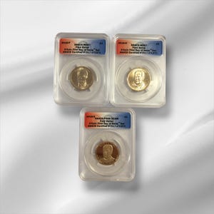 May include: Three gold Ford Dollar coins in clear protective cases. Each coin features a portrait and is labeled with "Ford Dollar" and "3-Coin First Day of Issue Set". The cases have labels with "ANACS Certified" and other details.