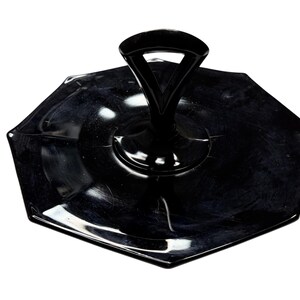 May include: A black glass serving tray with an octagonal shape and a central arched handle. The surface of the tray is smooth and reflective, featuring a raised rim and a solid black color throughout the entire piece.