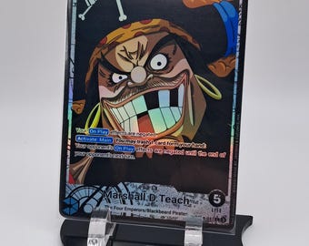 May include: A collectible trading card featuring a cartoon illustration of Marshall D. Teach, also known as Blackbeard, from the anime series One Piece. The card has a holographic finish and a black background with a skull and crossbones design. The card's text reads "Your On Play effects are negated. Activate Main: You may trash 1 card form your hand: Your opponent's On Play effects are negated until the end of your opponent's next turn. Marshall D. Teach. The Four Emperors/Blackbeard Pirate. 5 Life."