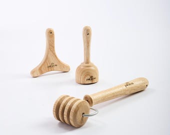 May include: Three wooden massage tools: a roller with a wooden handle, a small wooden cup with a handle, and a wooden tool shaped like a triangle with a handle. All tools have the word "Palmarosa" printed on them.