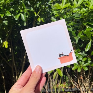 May include: A white ceramic mug with a black handle and the text "But First, Coffee" in a bold, black font. The mug is sitting on a wooden surface. The mug is 10 cm tall.