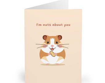 May include: A greeting card with a cartoon hamster holding a peanut. The card has the text "I'm nuts about you" in brown letters on a light peach background. The hamster is brown, white, and tan.