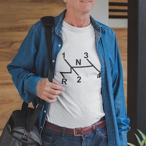 Könnte beinhalten: Weißes T-Shirt mit einem schwarzen Schaltmuster. Das Shirt hat die Zahlen 1, 2, 3, 4 und R sowie den Buchstaben N. Die Person trägt ein Jeanshemd und Jeans.