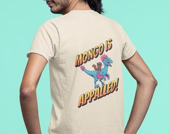 May include: A cream-colored t-shirt with a cartoon image of a blue dinosaur with a pink mohawk riding a brown and white creature. The text "MONGO IS APPALLED!" is printed in yellow and orange letters.