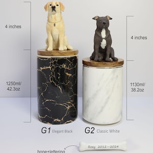 May include: Two ceramic pet urns with dog figurines on top. The urn on the left is black with gold marble pattern and says "G1 Elegant Black" and "1250ml/42.3oz". The urn on the right is white with a marble pattern and says "G2 Classic White" and "1130ml/38.2oz". A white bone with the text "Roxy 2012-2024" is in the bottom right corner.