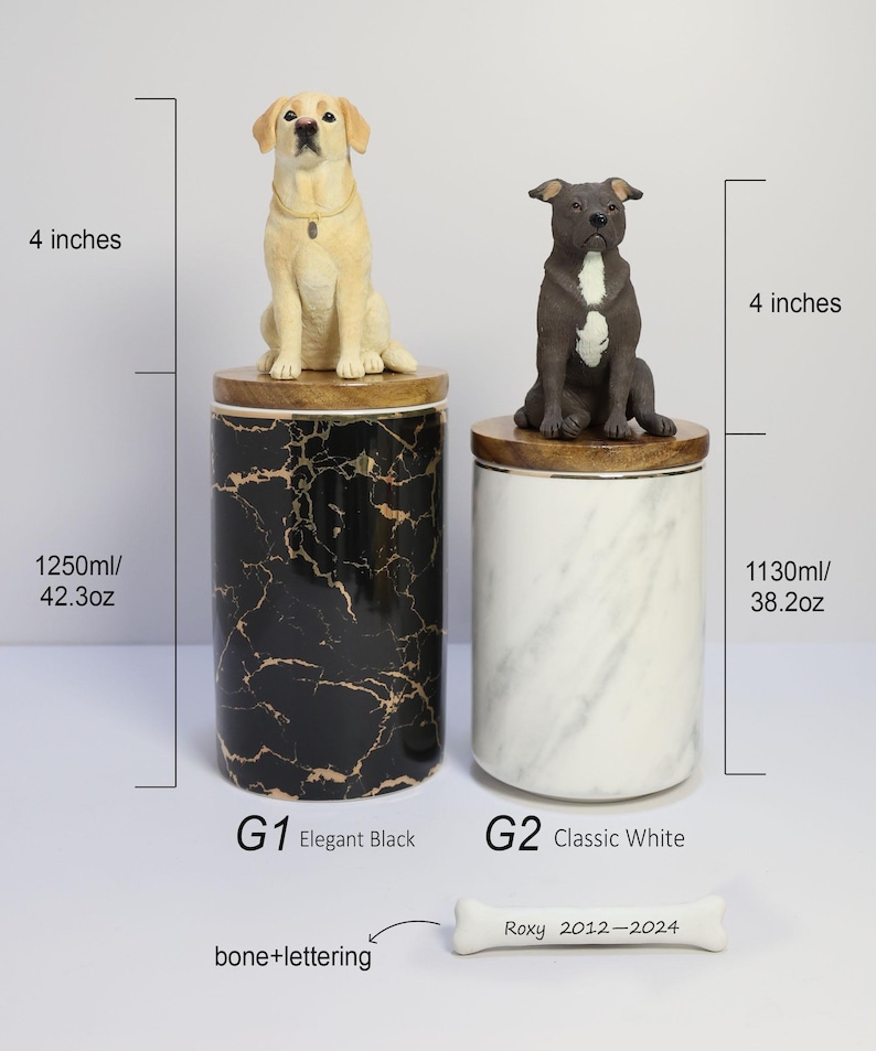 May include: Two ceramic pet urns with dog figurines on top. The urn on the left is black with gold marble pattern and says "G1 Elegant Black" and "1250ml/42.3oz". The urn on the right is white with a marble pattern and says "G2 Classic White" and "1130ml/38.2oz". A white bone with the text "Roxy 2012-2024" is in the bottom right corner.
