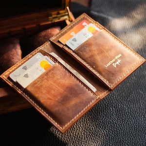 May include: Open brown leather wallet with multiple card slots, filled with credit cards. The wallet has a stitched border and the text "Leather-Man Dapp" is visible. The wallet is open, revealing the interior and cards.