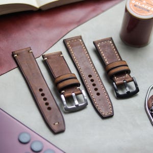 Könnte beinhalten: Vier braune Lederarmbänder mit kontrastierenden Nähten und Metallschnallen. Ein Armband hat eine schwarze Schnalle, die anderen silberfarbene. Eine Garnrolle und ein Lederaccessoire sind ebenfalls vorhanden.