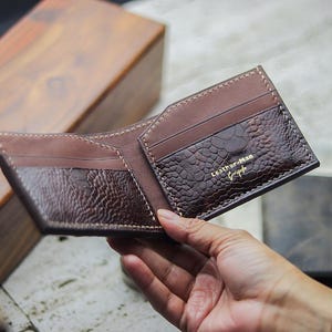 May include: A bi-fold wallet featuring a combination of smooth light brown leather and dark brown textured leather with a reptilian pattern. The interior includes multiple card slots and the gold embossed text Leather-Man on the right side.