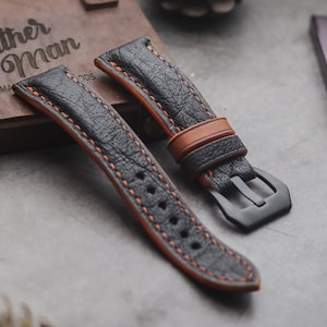 Pode incluir: Duas pulseiras de relógio de couro preto com costuras laranja. As pulseiras têm um fecho de fivela e são feitas de couro texturizado.